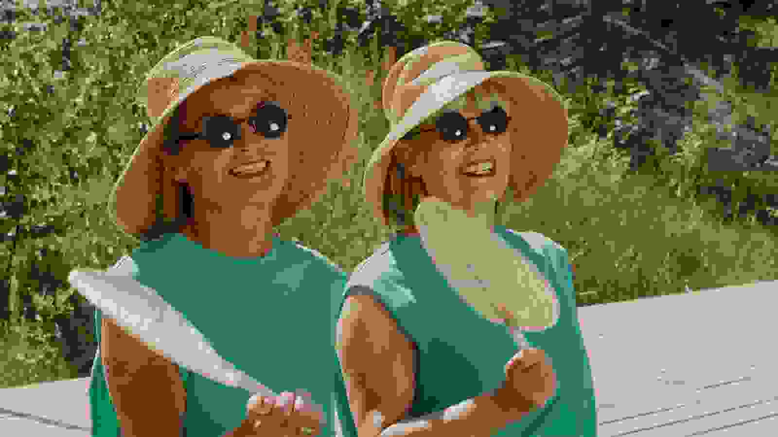 Två glada kvinnor i solhattar och solglasögon fläktar sig utomhus